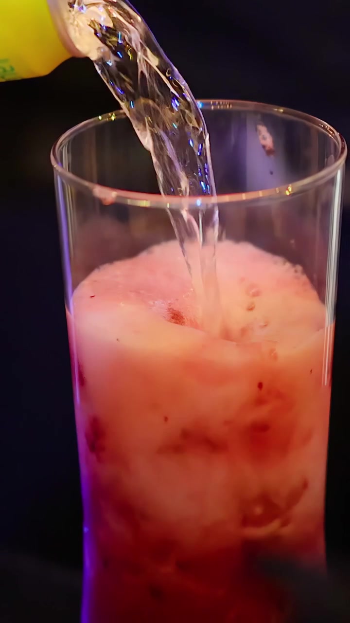 Limonata versata su ghiaccio e frutti rossi, mescolata in un bicchiere alto sotto un'illuminazione colorata.