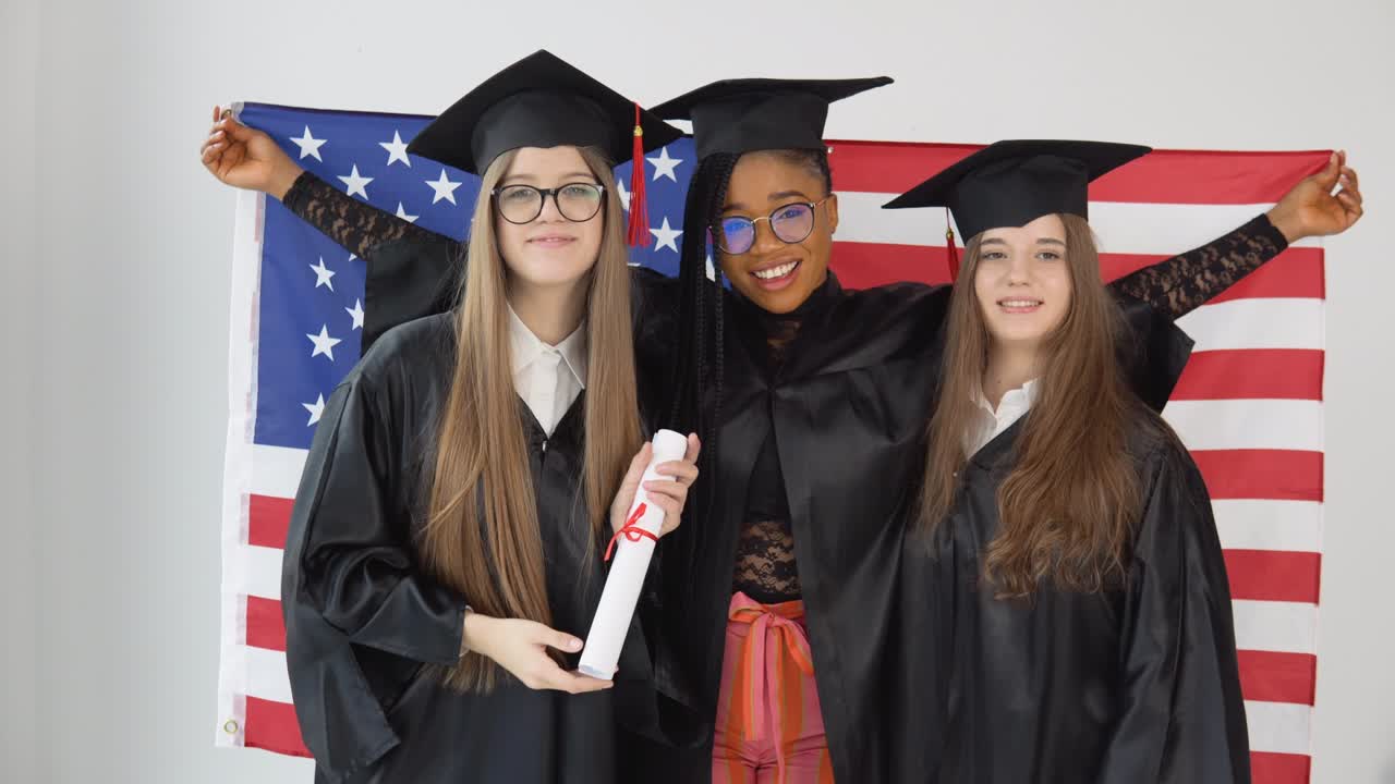 tres estudiantes femeninas de la universidad de ee.uu. llevan trajes y sombreros de graduación. una de ellas tiene un diploma de maestría