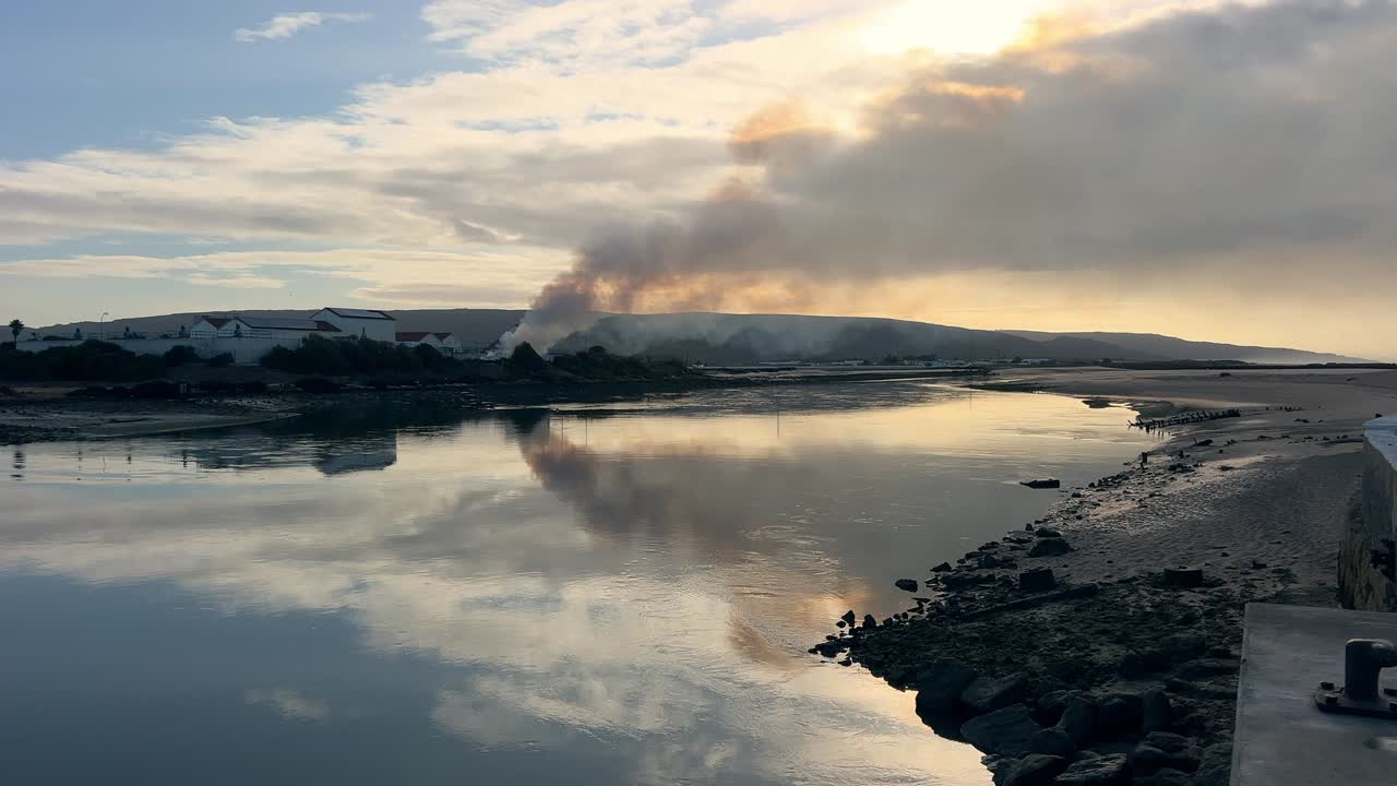 shot of a controlled fire burning in a rural field, with the faint skyline of a distant city visible on the horizon under a clear day