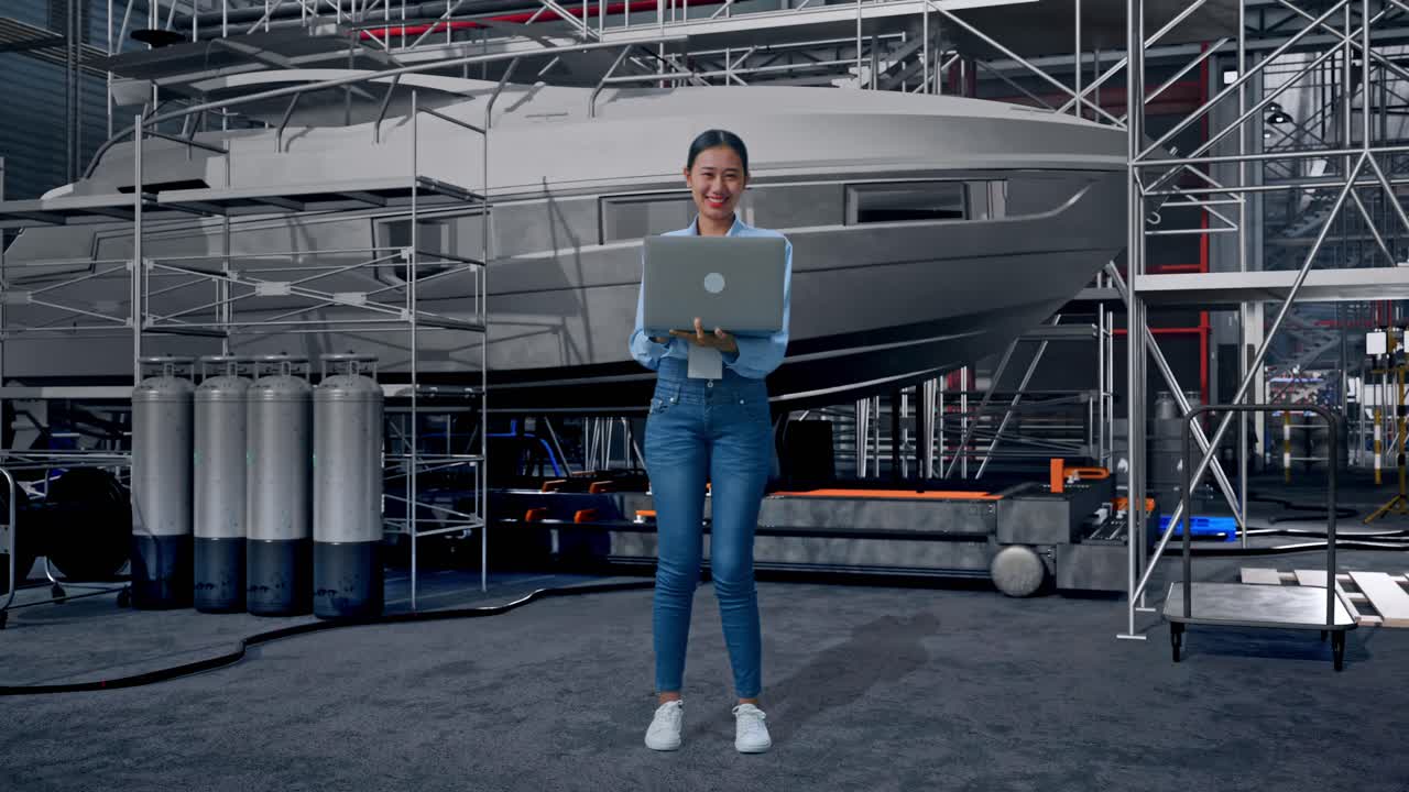 Full Body Of Asian Female With Her Laptop with Yacht Construction in Modern Shipyard, She Is Looking At The Camera With A Smile