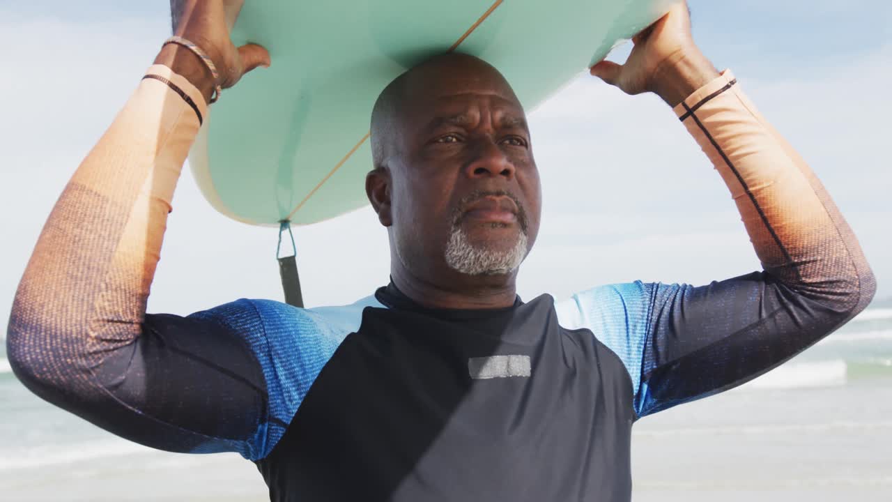 African american senior man walking on a beach holding surfboard on his head