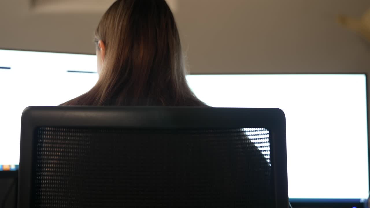 Back View of Woman Working at Office Desk with Monitors, Left to Right