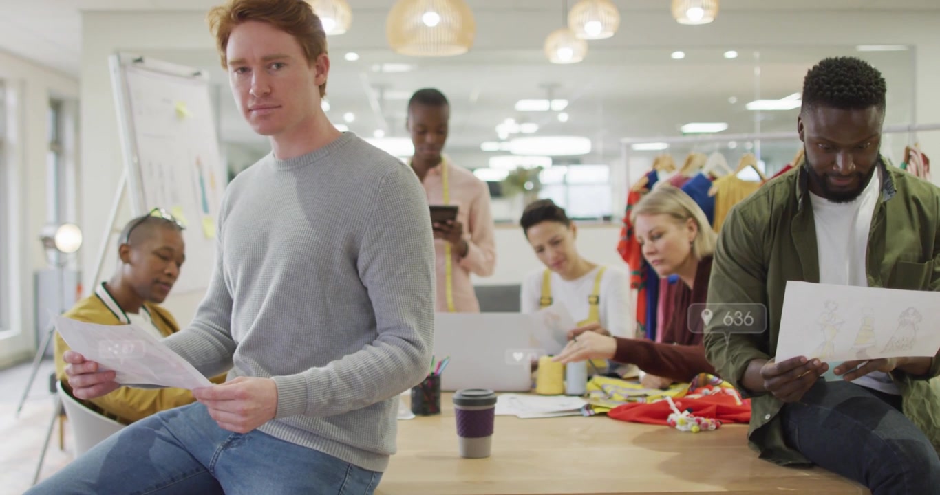 Designteam samles ved et bord, en mand læser ark, en telefon viser animerede målinger, der guider gennemgangen.