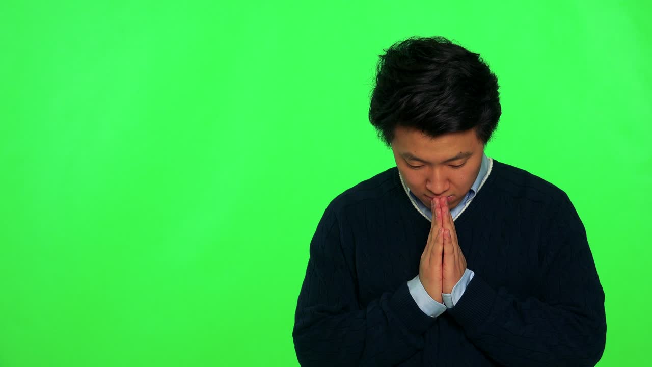 un joven asiático reza con las manos juntas - estudio de pantalla verde