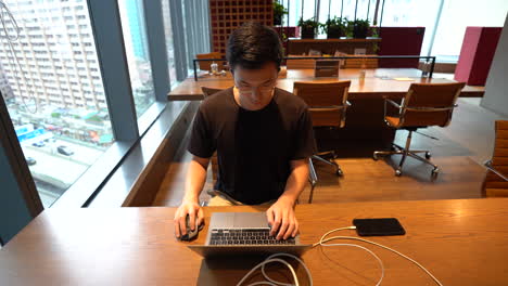 chinese asian millennial with glasses working on laptop in empty co-working space in hong kong