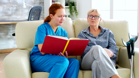 caucasian female assistant in nursing home reading a book to an elderly retired woman