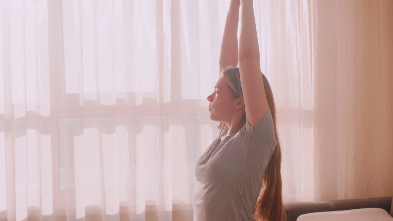 Remote designer sits on sofa stretching arms backward and adjusting hair in soft morning light, engaging in calming shoulder movement for posture relief and relaxed home based workflow transition