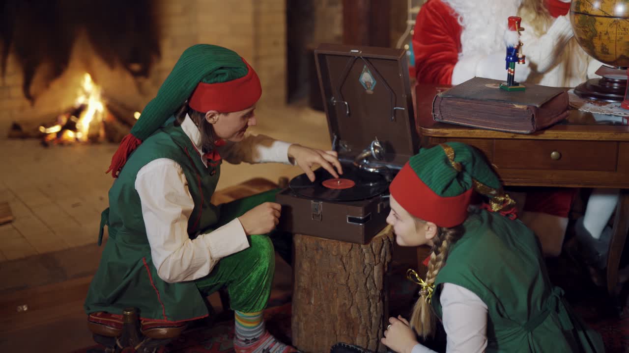 Curious elves with retro recorder indoors. Elves in festive costumes playing with old recorder with disks at Christmas.