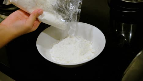 pouring white flour from plastic bag into bowl, close up