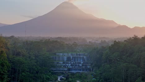 indonesia landscape with mountain silhouette and waterfall during sunrise, aerial view