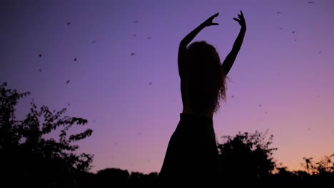 connecting with nature - a beautiful woman dancing to the tune of the purple heaven during sunset with bats flying overhead