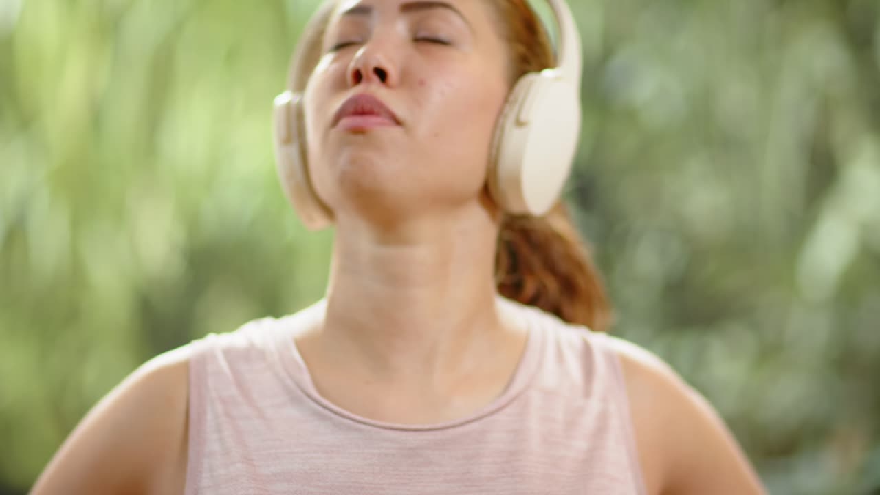 Donna che si mette cuffie over-ear bianche a casa, con un top senza maniche rosa pallido, preparandosi ad ascoltare