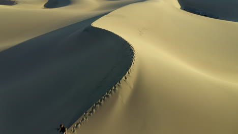 imágenes de drones de un hombre caminando a través de dunas de arena vacías al amanecer en el desierto