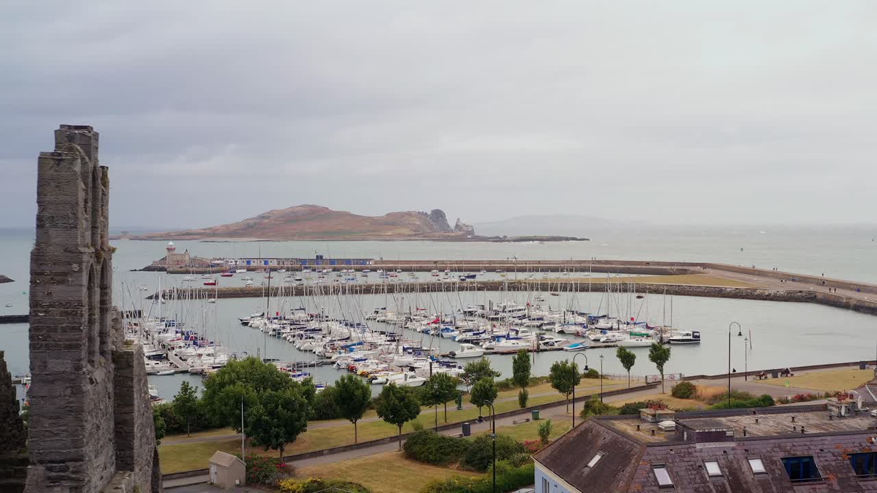 Drone ascends along broken exposed walls and facade of Howth Abbey to reveal Ireland's Eye