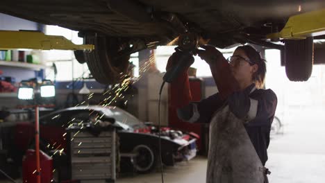 Female-mechanic-using-electric-blade-cutter-and-working-under-a-car-at-a-car-service-station