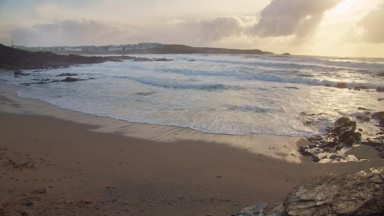olas espumosas salpicando en la orilla al atardecer en la pequeña playa fistral, newquay, inglaterra - vista amplia