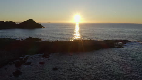 aerial dolly shot of tourists silhouetted against the calm ocean at giant's causeway, capturing the warm sunset backdrop