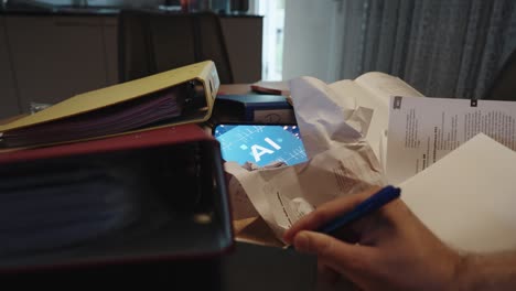 a table with papers, books, and folders, and a hand writing on a sheet