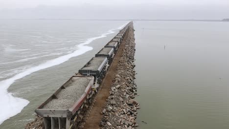 forward aerial of freight train transporting stone by water, argentina