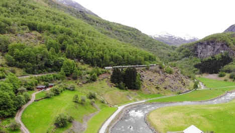 aerial: flåm train going uphill through by a mountain side in a valley