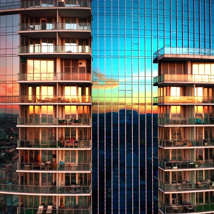 Mirror windows of modern multi-storied high-rise block of flats reflecting beautiful light at sunset. Drone flying around the building at sundown.