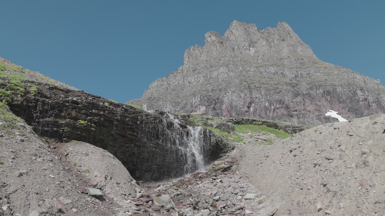 Waterfall and mountain landscape at Logan Pass, Montana under clear skies