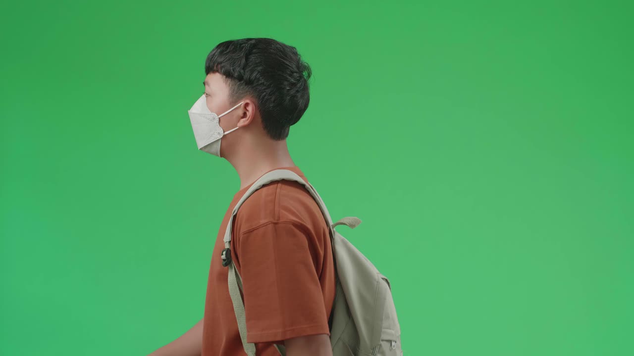 The Side View Of Asian Boy Student Wearing A Mask And Backpack Walking To School On Green Screen Chroma Key.