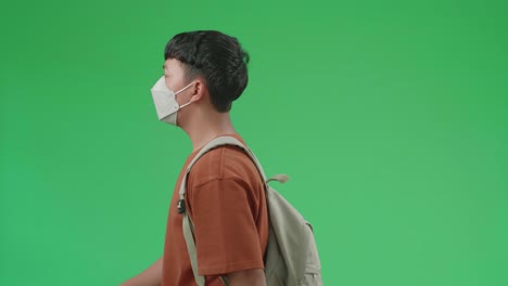 the side view of asian boy student wearing a mask and backpack walking to school on green screen chroma key.