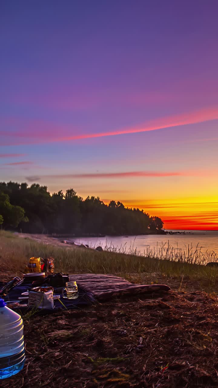 Vertical time lapse of a couple on a romantic picnic by a lake at sunset with motion blur showing their movement against a vibrant orange sky
