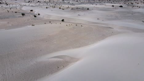 Drone-shot-flying-over-dunes-in-the-Tatón-desert-in-Catamarca,-Argentina-while-panning-up-to-reveal-mountains-in-the-distance