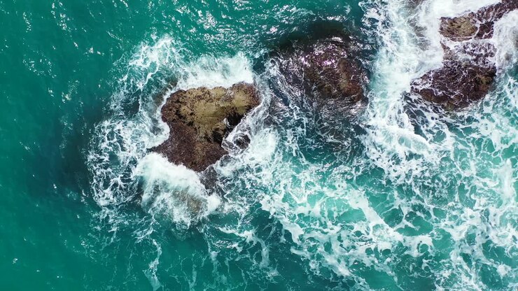 Onde oceaniche che si infrangono sulle scogliere, spargendo goccioline nell'aria, paesaggio drammatico con acqua turchese che spumeggia alle Hawaii.
