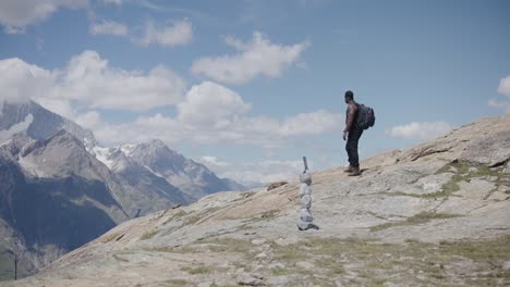 black male traveler with backpack thinking about god and crossing himself while looking up mountainside near the matterhorn in switzerland