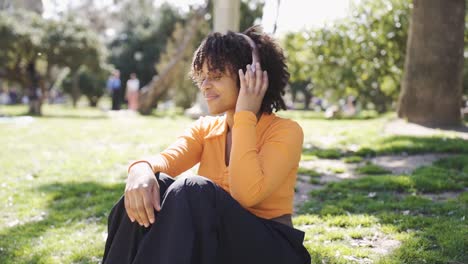 mujer negra tranquila escuchando música en auriculares en el césped