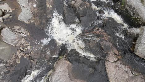 Agua-Corriente-Marrón-Que-Fluye-En-El-Paisaje-Rocoso-En-Las-Montañas-Wicklow,-Irlanda---Drone-Aéreo