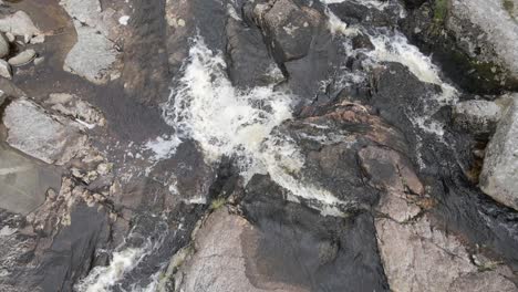 brown stream water flowing on the rocky landscape in the wicklow mountains, ireland - aerial drone