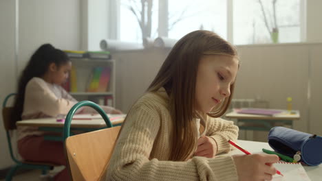 Schoolgirl-learning-in-classroom.-Cheerful-pupil-sitting-at-desk-during-lesson