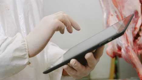 butcher using digital tablet in meat storage room