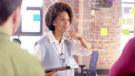 biracial creative businesswoman with tablet in casual meeting with diverse colleagues, slow motion