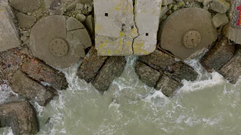 aerial birdseye view of abandoned seaside fortification buildings at karosta northern forts, baltic sea coast , large waves, overcast day, slow motion, ascending drone shot