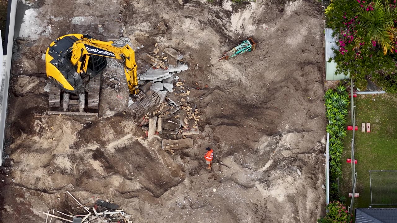 Overhead drone shot of heavy machinery moving earth and concrete rubble at a residential site.
