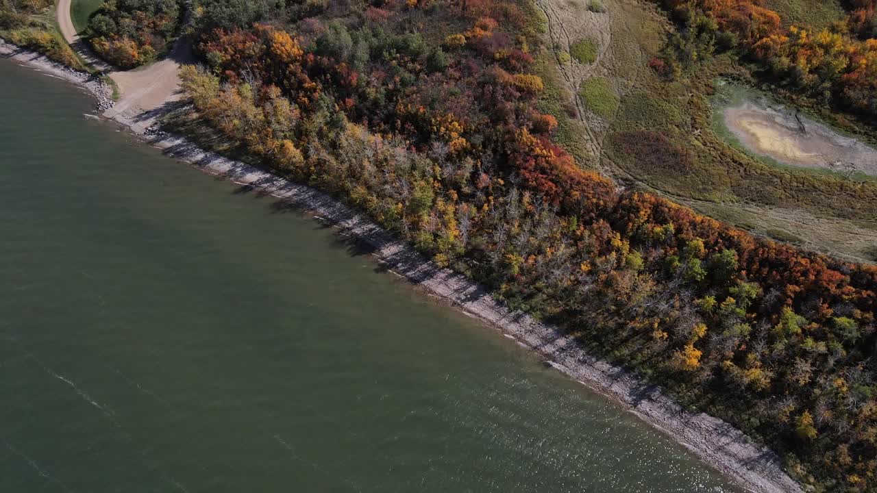 imágenes aéreas que se mueven lentamente hacia los lados con cardán hacia arriba que revelan el lanzamiento del barco, el follaje otoñal y las cabañas frente al lago a lo largo de la costa