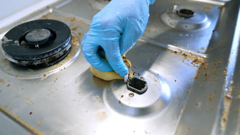cleaning kitchen stove with care. a person wearing a blue glove scrubs a dirty stove surface, removing food residue and stains effectively