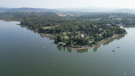 línea de costa de un tranquilo lago de montaña en las montañas beskid, rodeado de vegetación durante un día de verano - vista aérea 4k