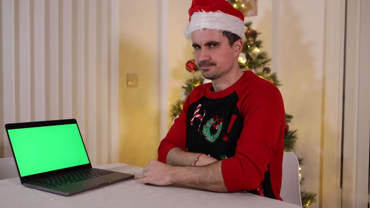 hombre caucásico mirando la computadora portátil de pantalla verde con decepción e incredulidad durante la reunión de vacaciones de navidad en su oficina en casa con un árbol de navidad en el fondo