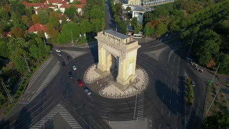A-Bird’s-Eye-View-of-Bucharest-at-Sunrise:-Rotating-Drone-Footage-of-the-Arch-of-Triumph-and-Passing-Cars,-Arcul-De-Triumf,-Romania,-Europe
