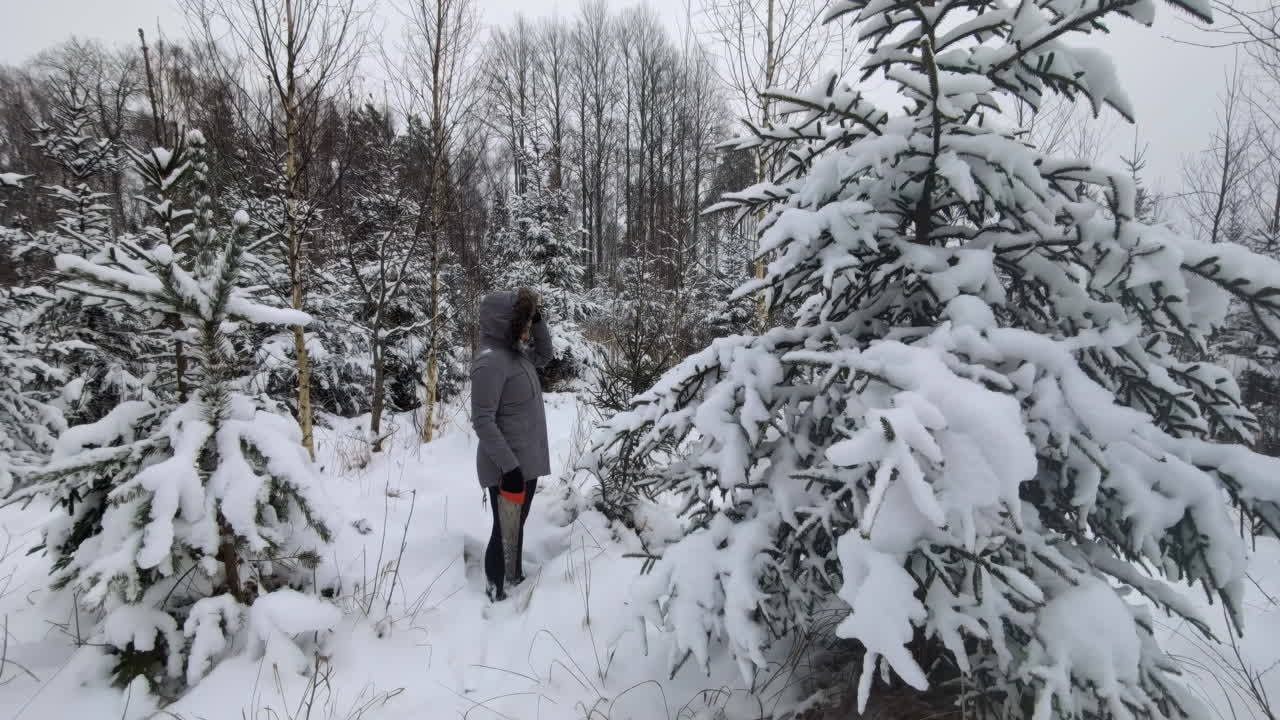 una mujer con una sierra caminando en un bosque cubierto de nieve en un clima nublado