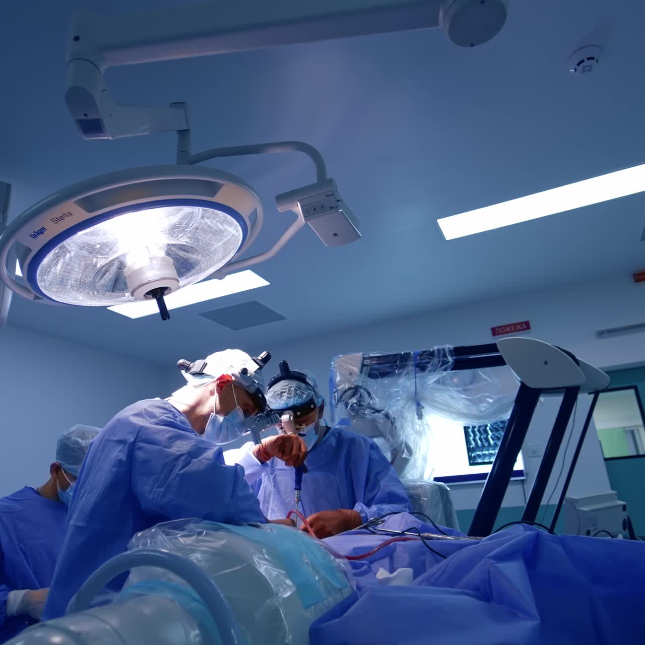 Two neurosurgeons working in modern surgery room. Doctor uses screwdriver at his work. Assistant arranging tools and instruments