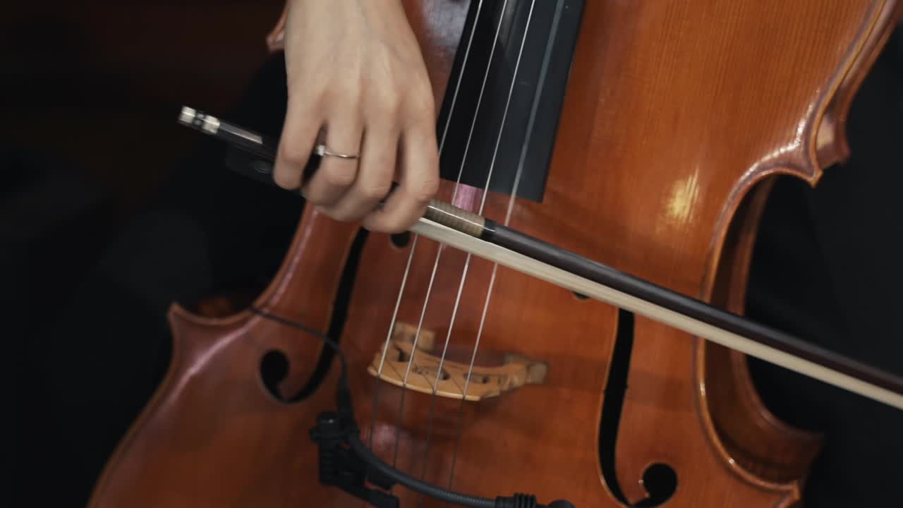 primer plano de un músico tocando un violonchelo con un arco, destacando las cuerdas y el cuerpo de madera