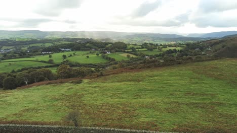 Sunbeams-moving-across-overcast-British-agricultural-rural-village-countryside-morning-aerial-panning-slow-left-view