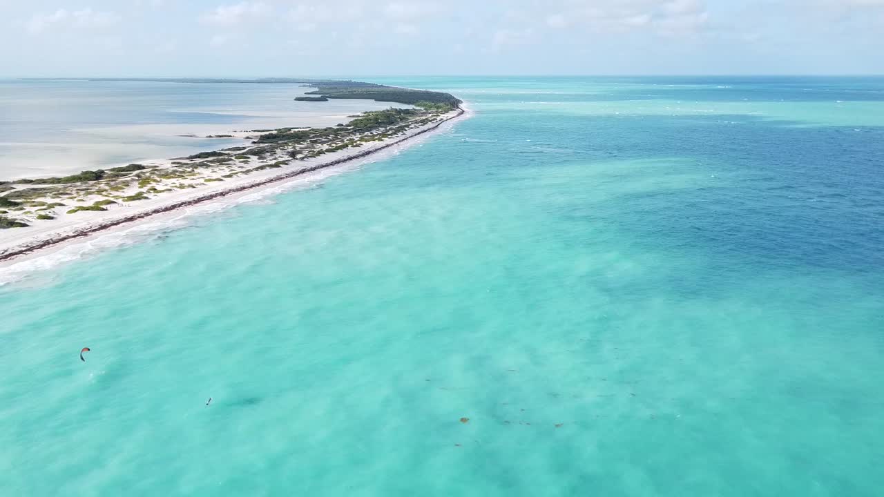 Vedute aeree con drone delle acque azzurre e turchesi del Mar dei Caraibi a Isla Blanca, Cancun, Messico, mentre un kitesurfer vola sopra l'acqua blu incontaminata che lambisce la spiaggia bianca
